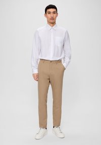 White button-up shirt with a chest pocket, paired with tan tailored pants and white sneakers, featuring a smooth texture and slim fit.