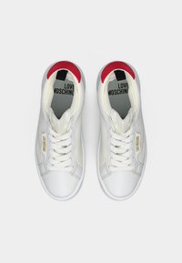 Λευκά αθλητικά παπούτσια Love Moschino με κορδόνια, πλευρές από δίχτυ και κόκκινες κάπες στη φτέρνα, σε θέα από πάνω σε απλό φόντο.