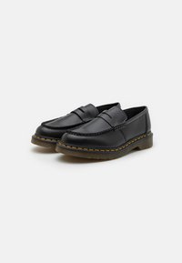 Sorte skinnslippers med et mokkasinlignende design, som har en flettet aksent og gule sting langs sålen.