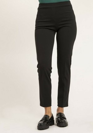 Pantalons noirs cintrés à taille haute, texture lisse et design de jambe fuselée. Associés à des mocassins noirs brillants.