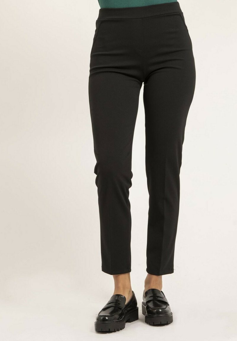 Pantalons noirs cintrés à taille haute, texture lisse et design de jambe fuselée. Associés à des mocassins noirs brillants.
