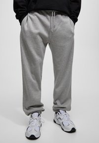 Grijze sweatpants met een elastische tailleband en trekkoord, voorzien van zijzakken, in combinatie met wit en zwart sport schoenen.
