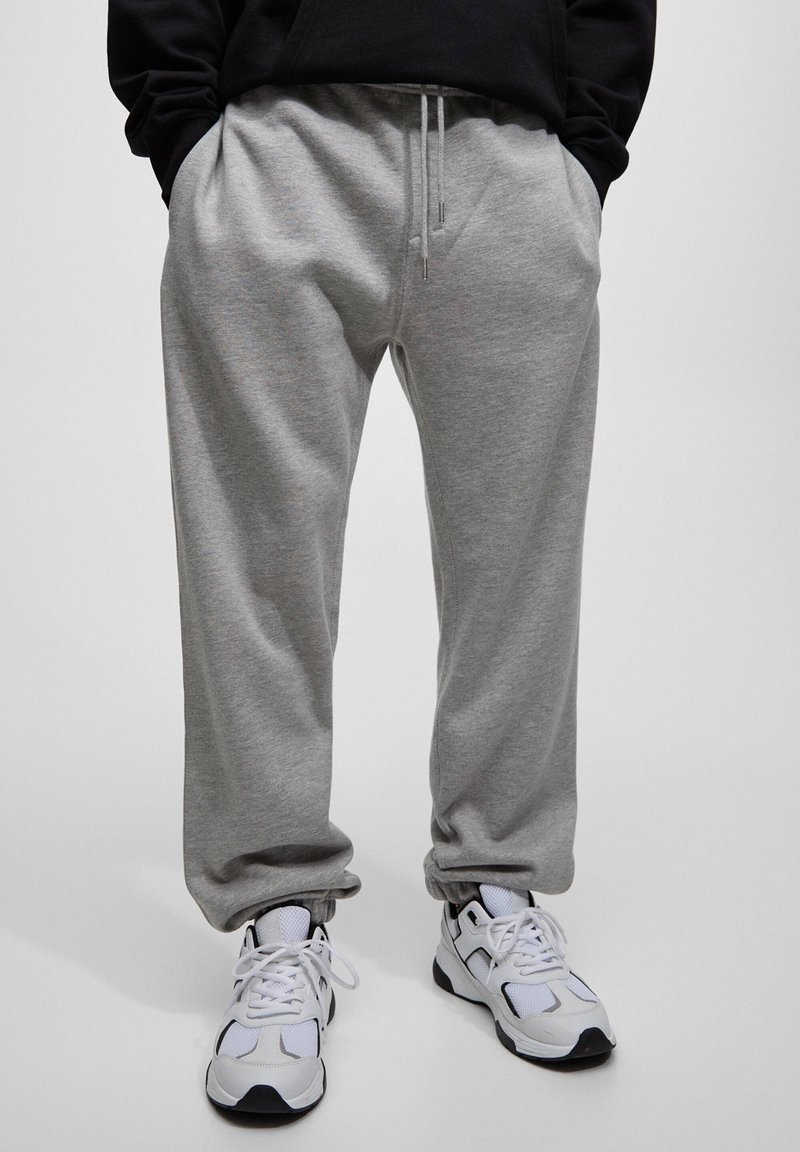Grijze sweatpants met een elastische tailleband en trekkoord, voorzien van zijzakken, in combinatie met wit en zwart sport schoenen.