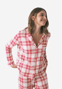 Set di pigiama a quadri rossi e bianchi realizzato in morbido cotone, composto da una camicia con bottoni e tasca e pantaloni abbinati.