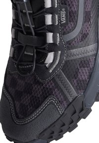 Gros plan d'une basket Vans noire et gris foncé montrant les lacets, la texture du tissu, les coutures et une partie de la semelle en caoutchouc.