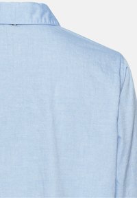 Chemise bleu clair à manches longues, vue de dos montrant le col et la partie supérieure des épaules sur un fond blanc uni.