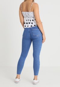 Top blanco con lunares negros, cuerpo fruncido, acompañado de jeans skinny de talle alto azules con dobladillos deshilachados y zapatillas blancas.
