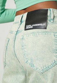 Light blue, high-waisted jeans with a faded texture. Black logo tag reading "KARL LAGERFELD JEANS" on the back. Features rear pockets.