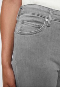 Jeans de mezclilla gris con un diseño estándar de cinco bolsillos, costuras visibles y una textura elegante y suave. Vista cercana de la zona de la cadera.