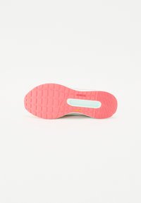 De buitenzool van de sportieve schoen heeft een felle roze rubber met een getextureerd grippatroon en een kleine aqua-accent bij de hiel. Merken in het geel.