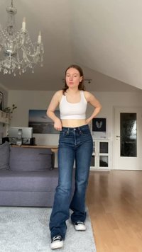 Kék farmer bővülő szárú nadrág magas derekkal, fehér crop top-pal párosítva. Az anyaga sima, és a nadrág öt zsebbe van ellátva.