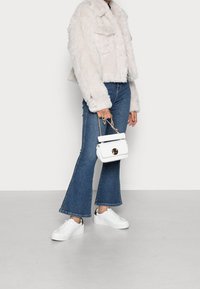 Faux fur kort jacka i ljusbeige, kombinerad med utsvängda blå jeans och vita sneakers. Liten vit handväska med gulddetaljer.