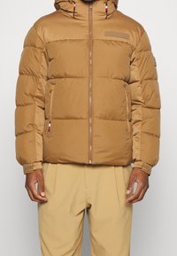 Brown puffer jacket with a hood, featuring a front zipper, elastic cuffs, and logo patch. Smooth texture with quilted design and side pockets.