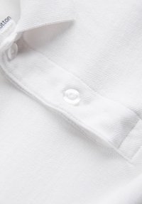 Biała bawełniana koszulka polo, z detalami takimi jak fakturowany materiał, klasyczny kołnierzyk oraz widoczny guzik o gładkiej powierzchni.