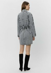 Grå denimklänning med bälte i midjan och långa ärmar. Har en strukturerad krage och elastiska detaljer på baksidan. Stylead med svarta knähöga stövlar.