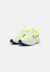 Nike athletic shoes in white with neon yellow accents. Mesh upper, cushioned sole, and black rubber outsole. Features contrasting logo detail.