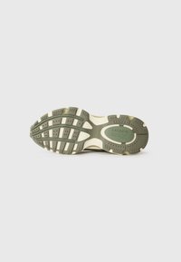 Sola de sapatilhas verde e bege com borracha texturizada, apresentando um design em camadas, sulcos para tração e o logótipo da Lacoste no centro.