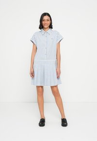 Φόρεμα με γαλάζιες και λευκές ρίγες, κοντά μανίκια, εμπρόσθιο κουμπί και φούστα με φουσκωτή γραμμή. Διαθέτει αντίθετη οριζόντια ρίγα στη μέση.