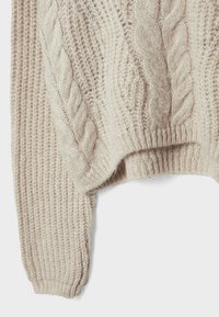 Sweter z plecionym wzorem w jasnym beżu, z prążkowanymi mankietami i dołem, miękka tekstura oraz luźny krój z opadającymi ramionami.
