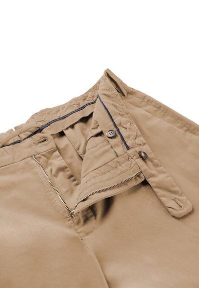 Pantaloni beige con cerniera parzialmente aperta e fascia in vita abbottonata, distesi, che mostrano il dettaglio della fodera interna blu.
