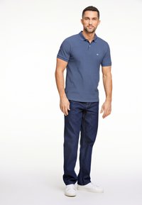 Camisa polo de algodón azul con tapeta de dos botones, combinada con jeans de denim azul oscuro y zapatillas blancas. Diseño sencillo y corte relajado.