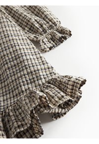 Tissu à carreaux marron et crème avec des poignets et un ourlet à volants, mettant en valeur un motif texturé et un design ludique.