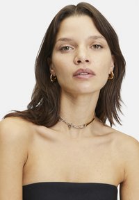 Gold- und Silber-Choker-Halskette mit einem Verschlussdesign, das eine Mischung aus Kette und schlanken Metallakzenten auf nackter Haut zeigt.