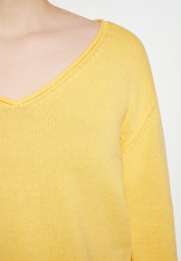 Maglione giallo a maglia con scollatura a V, tessuto testurizzato e bordi a coste. Le maniche sono leggermente scese con un fit rilassato.