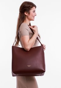 Brown leather tote bag with a smooth texture, featuring a subtle embossed logo, designed with a spacious, minimalist shape and adjustable strap.