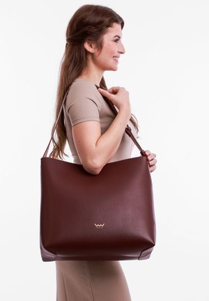 Brown leather tote bag with a smooth texture, featuring a subtle embossed logo, designed with a spacious, minimalist shape and adjustable strap.