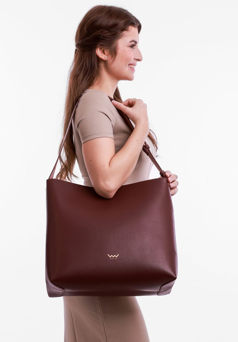 Brown leather tote bag with a smooth texture, featuring a subtle embossed logo, designed with a spacious, minimalist shape and adjustable strap.