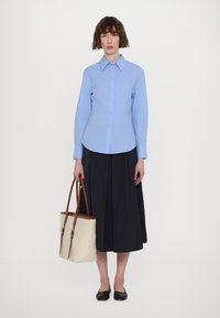 Camicia azzurre chiaro con maniche lunghe, abbinata a una gonna nera. Borsa a tracolla beige con manici marroni. Scarpe nere basse.