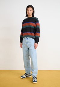 Gestreept langearmen overhemd in zwart, groen, roest en blauw. Blauwe jeans, relaxed fit. Sneakers met marineblauwe, witte en lichtgrijze accenten.