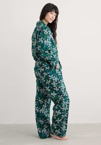 Lillelilleke mustriga pidžaama, mis sisaldab rohelisi ja halli toone, laia lõikega, pikkade käistega ja kaelusega.