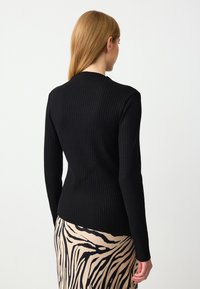 Zwart geribbelde lange mouw top met een aansluitende silhouet. De achterkant heeft een hoge halslijn en is gecombineerd met een geblokte rok.