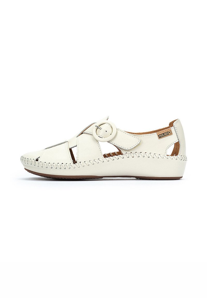 White leather shoe with cutout design, circular hardware accent, stitched detail along the sole, and a tan interior lining.