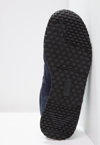 Sole z námořnického semiše s texturovanou černou gumou, která má charakteristický vzor podrážky a logo "ARMANI".