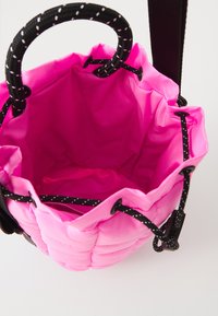 Borsa a cordoncino imbottita di colore rosa acceso con maniglie in corda nera e bianca, con apertura superiore che mostra l'interno vuoto su uno sfondo bianco.