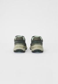 Athletic shoes with a dark green mesh upper, light green accents, and a chunky beige sole; features a textured finish and reinforced heel support.
