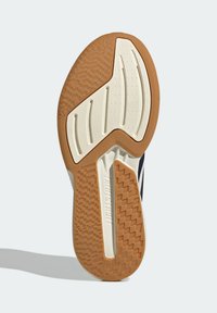 Semelle d'une chaussure de sport montrant des motifs de bande de roulement en caoutchouc marron et blanc, avec le mot "LIGHTSTRIKE" embossé sur la semelle intermédiaire.