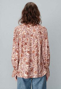 Blouse à motif floral en crème clair avec des nuances de bordeaux et de rouille. Manches longues, coupe ample et détail froncé au dos.