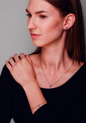 Das silberne Schmuckset umfasst ein herzförmiges Armband und eine Kette mit einem kreisförmigen Anhänger, beide mit zarten Kettendesigns.