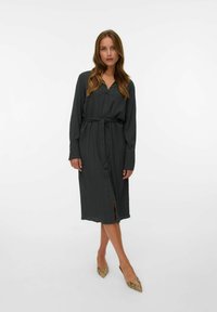 Robe chemise boutonnière vert foncé avec des manches longues et une ceinture à nouer. Présente des rayures verticales et une fente en bas. Tissu texturé.
