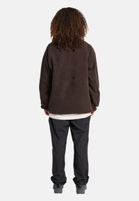 Brązowy polarowy sweatshirt o luźnym kroju z haftowanym napisem "ATW" na plecach, w zestawie z czarnymi spodniami i szarymi trampkami.