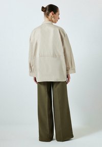 Beige overméretes dzseki hátvarrással, széles olajzöld nadrággal párosítva, sima anyagból készült.