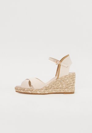 Sandali a zeppa in tessuto beige chiaro con suola in juta intrecciata, dotati di cinturino alla caviglia con fibbia e design incrociato sulla parte anteriore.