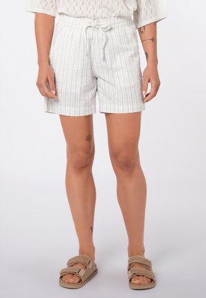 Person wearing white striped drawstring shorts, beige woven strap sandals, and a white knitted top, standing against a plain background.
