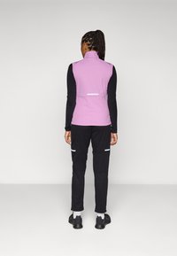Gilet sans manches violet sur une chemise noire à manches longues, associé à un pantalon noir avec des accents blancs et des motifs texturés.