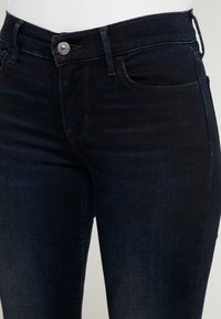 Jeans de mezclilla oscura con un diseño ajustado, bolsillos estándar y cierre con botón plateado. La tela tiene una textura suave con un desvanecido sutil.