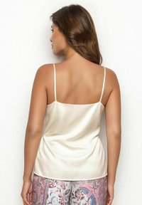 Camisola in satin color crema, con spalline sottili e una texture liscia, abbinata a pantaloni tapered a fantasia.